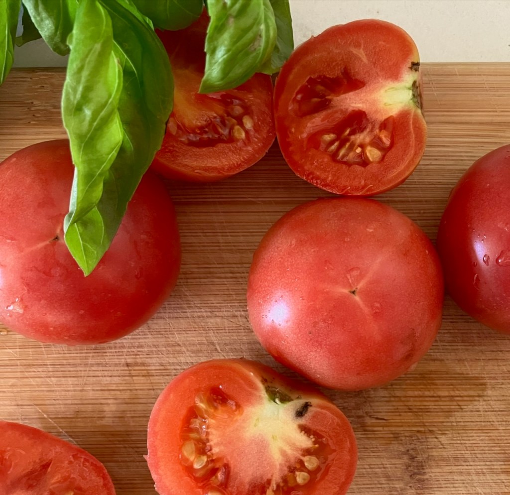 Runde rote Tomaten, ganz und halbiert, auf einem Holzbrett mit Basilikumblättern