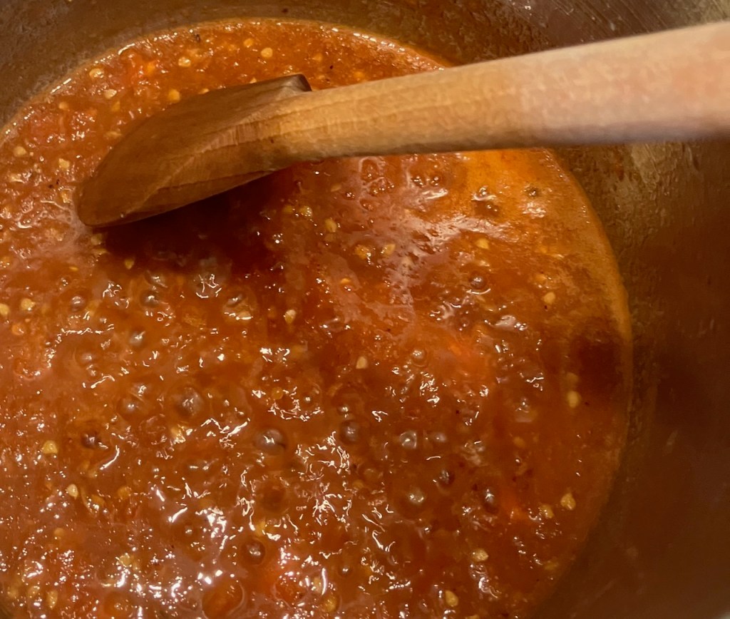 Tomatensauce kocht im Topf, ein Holzlöffel rührt um