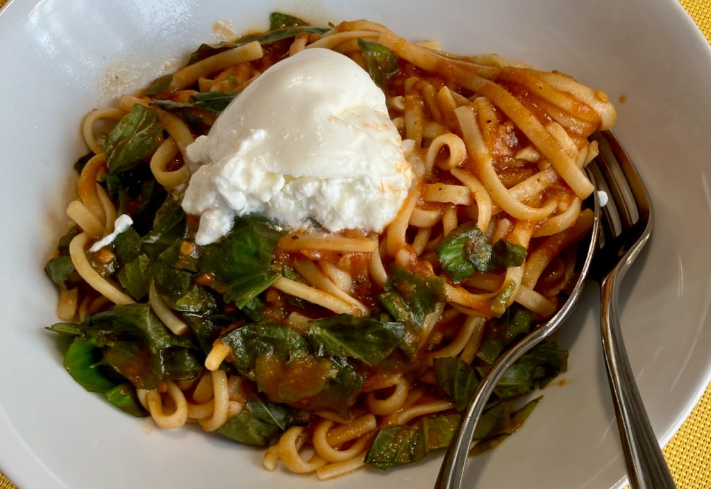 Angerichtete Linguine mit Burrata auf einem tiefen Teller, daneben eine Gabel